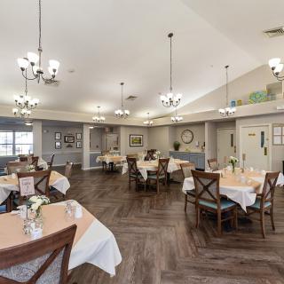 A spacious and elegantly decorated dining area with neatly arranged tables and chairs, featuring chandeliers overhead.