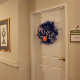 A decorated door in a hallway with a blue wreath and artwork on the wall.