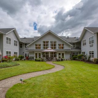 A large residential building with a manicured lawn and a winding pathway under a cloudy sky.