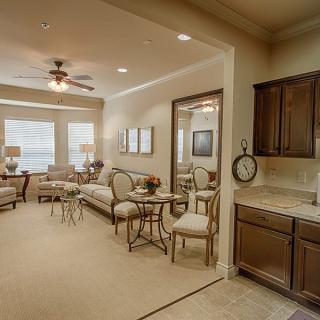 A cozy and elegantly furnished living room with a neutral color palette, featuring a sofa, chairs, tables, and a ceiling fan.