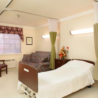 A well-lit and comfortable hospital room featuring a patient bed, a sofa for visitors, and natural light from the window.