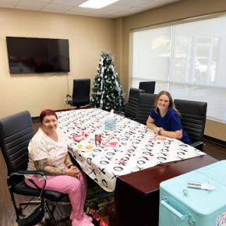 Two women sitting at a festive table in an office with a decorated Christmas tree.