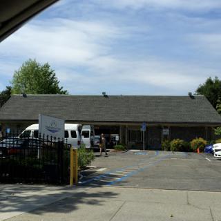 A view of a building with vehicles parked in front, surrounded by trees under a partly cloudy sky.
