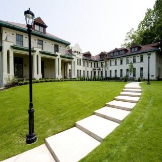 A grand mansion with a well-maintained lawn and a stone pathway leading to the entrance.