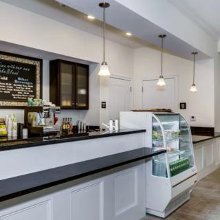 A modern cafe with a sleek counter and display case, featuring a menu board and pendant lighting.
