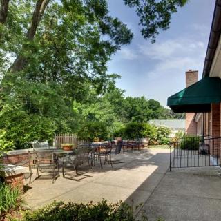 A sunny outdoor patio area with tables and chairs surrounded by lush greenery.