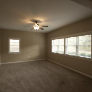An empty room with carpet flooring, several windows, and a ceiling fan.