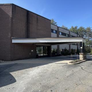 A modern commercial building with a covered entrance, surrounded by greenery on a clear day.