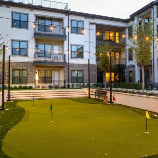 Modern apartment complex with a well-maintained putting green in the courtyard at dusk.