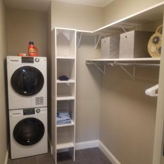 A tidy laundry room with a stacked washer and dryer, shelving units, and ample closet space.