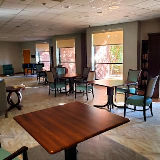 A cozy lounge area featuring chairs and tables, illuminated by natural light streaming through large windows.