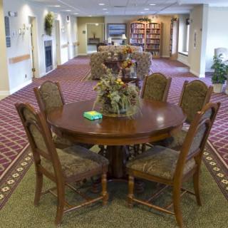 A well-furnished dining area with a round wooden table and six chairs, set on a patterned carpet.