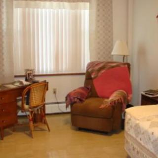 A cozy bedroom setup with a desk, chair, and an armchair beside a bed.