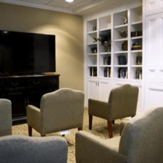 A cozy living room featuring a large television, several armchairs, and built-in bookshelves.