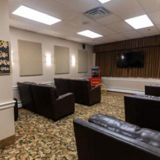 A comfortable lounge area with armchairs and a television, featuring a carpeted floor and bright lighting.