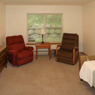 A cozy living room with two recliner chairs, a small table with a lamp, and a large window overlooking greenery.