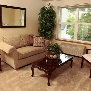 A cozy living room with a sofa, armchair, coffee table, and large window providing natural light.