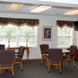 A cozy common area featuring tables and chairs, with ample natural light from large windows.
