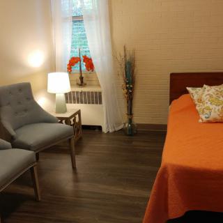 A cozy bedroom with a vibrant orange bedspread, two gray chairs, and a small side table with a lamp.
