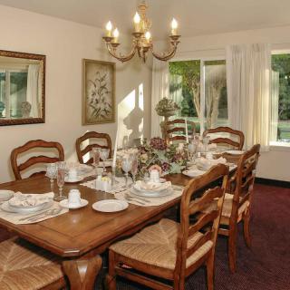 A traditional dining room with a wooden table set for a meal, featuring a chandelier and natural light from the windows.