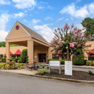A building entrance with landscaping and signage, featuring a parking area and flowering trees.