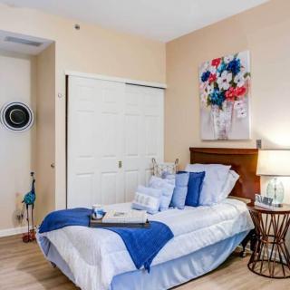 A cozy bedroom featuring a neatly made bed with blue and white bedding, complemented by wall art and a bedside lamp.