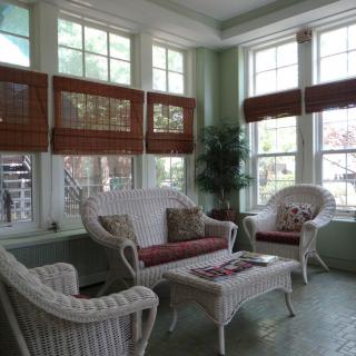 A cozy sunroom featuring wicker furniture, indoor plants, and abundant natural light.
