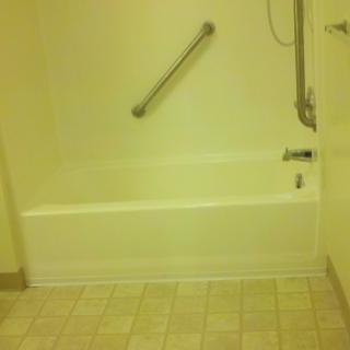 A bathroom with a bathtub featuring a grab bar and showerhead, tiled floor.