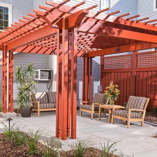 A wooden pergola in a backyard setting, featuring comfortable outdoor furniture and decorative plants.