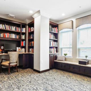 A cozy library corner with bookshelves, a desk, and large windows.