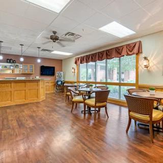 A cozy dining room with wooden flooring, round tables, and ample natural light.