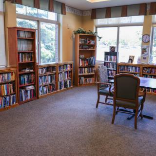 A cozy library with bookshelves and a reading table near large windows.