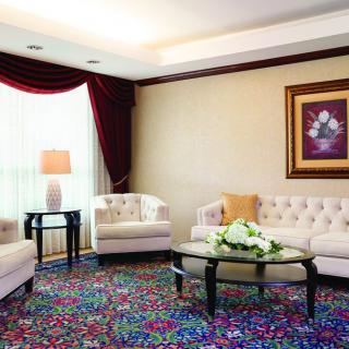 A cozy living room with elegant sofas, a vibrant carpet, and decorative artwork on the wall.
