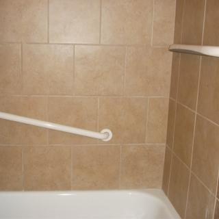 A tiled bathroom corner featuring a bathtub and a safety grab bar.
