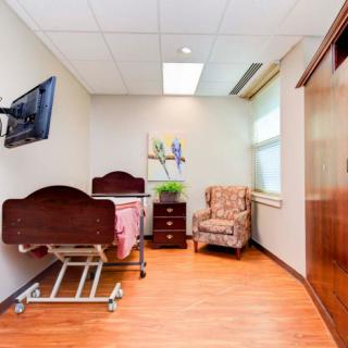 A neatly arranged hospital room featuring a medical bed, armchair, and mounted television.