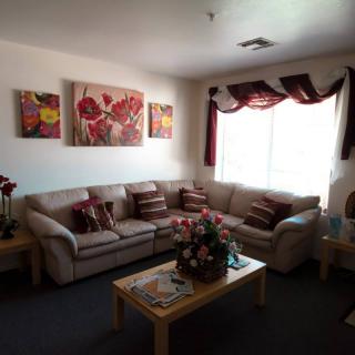A cozy living room featuring a sectional sofa, coffee table with a floral centerpiece, and decorative artwork on the walls.