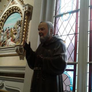 A monk gestures inside a church, surrounded by stained glass windows and religious artwork.