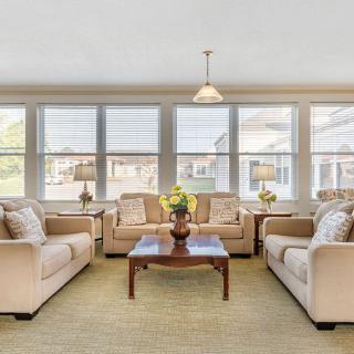 A bright and spacious living room with neutral-colored sofas and a wooden coffee table, surrounded by large windows.