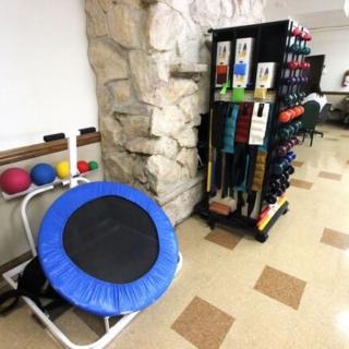 A corner of a fitness room featuring a small trampoline, medicine balls, and a rack of dumbbells.