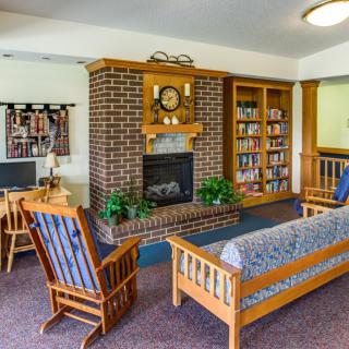 A cozy living room featuring a brick fireplace, wooden furniture, and a bookshelf.
