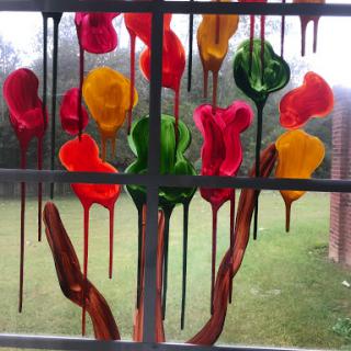 A vibrant display of colorful paint drippings resembling flowers on a window.
