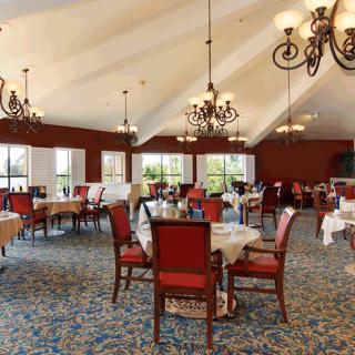 An elegant dining room with chandeliers, red chairs, and neatly arranged tables.