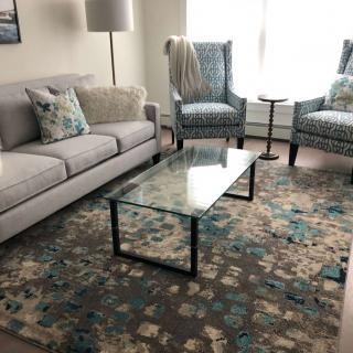 A cozy living room with a sofa, two armchairs, and a glass coffee table atop a patterned rug.