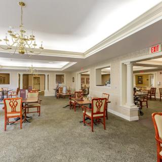 A spacious dining area with elegant chairs and tables, featuring a chandelier and detailed ceiling design.