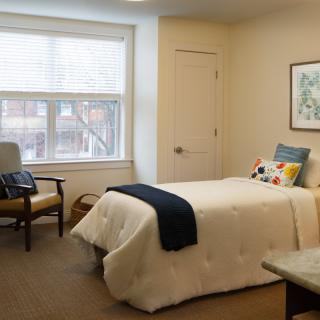 A cozy bedroom with a single bed, a large window, and comfortable furniture.