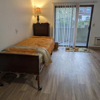 A cozy bedroom featuring a single bed with an orange blanket, complemented by a lamp and a sliding door that leads to the outside.
