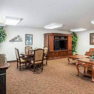 A cozy living area featuring traditional furnishings, a dining table, entertainment center, and indoor plants.