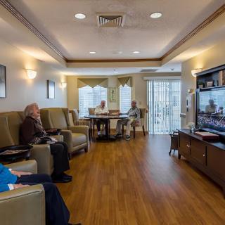 Elderly residents sit in a comfortable living room watching television in a retirement home.