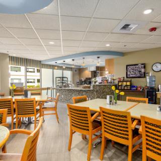 A bright and modern dining area featuring wooden tables and chairs, with a view of the kitchen.