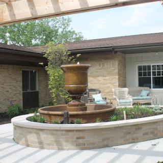 A serene outdoor space featuring a beautiful fountain surrounded by lush greenery and comfortable seating.